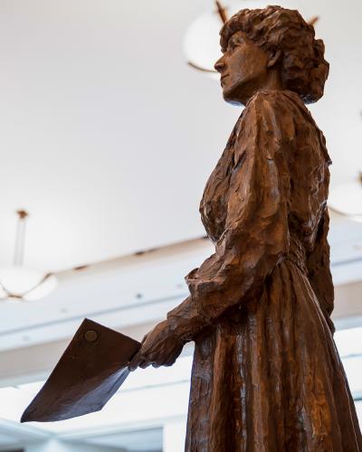 bronze bust of a woman wearing a dress and holding a piece of paper
