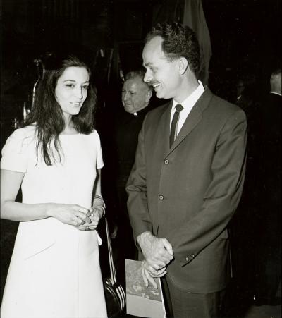 black and white photo of a woman in a white dress talking to a man in a suit to her right