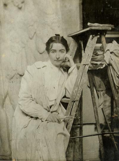 sepia photo of a woman staring at the camera with a dress on and leaning on a ladder