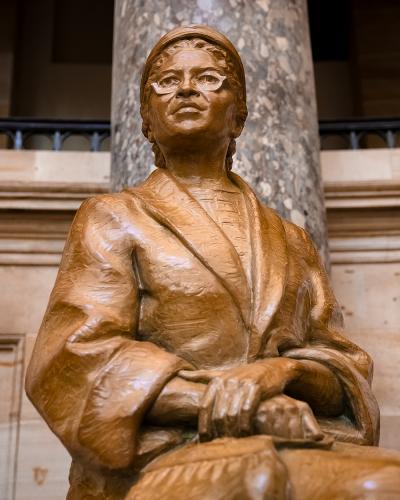 bronze statue of rosa parks sitting and looking off into distance wearing glasses and a hat