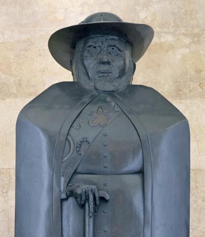 grey statue of a man with a hat and cloak