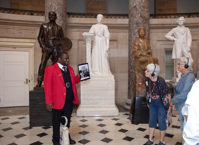 a tour guide in a red jacket and an elderly couple stand in front of the statues in the rotunda and glance over at them