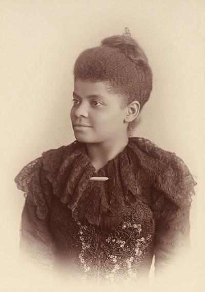 sepia photo of a woman staring to the left wearing her hair up and wearing a black lace frill-collared dress