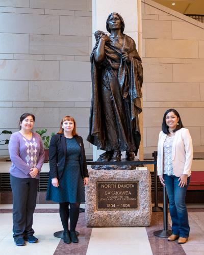 three women standing in front of a large bronze statue of the woman holding her baby on her back
