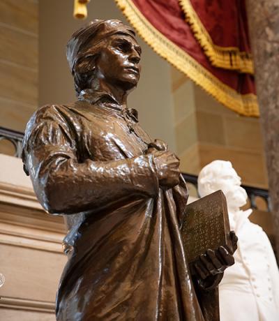 bronze statue of a woman with a long dress holding a book and looking straightforward