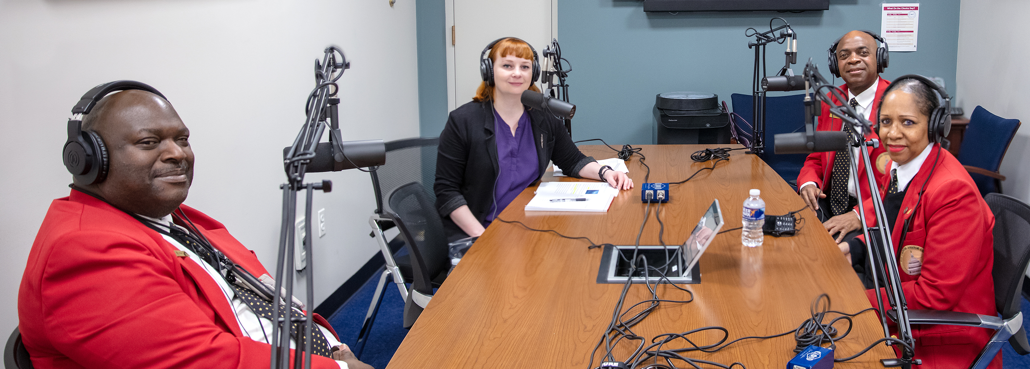 two men and two women in red jackets sitting around a table smiling all in front of microphones