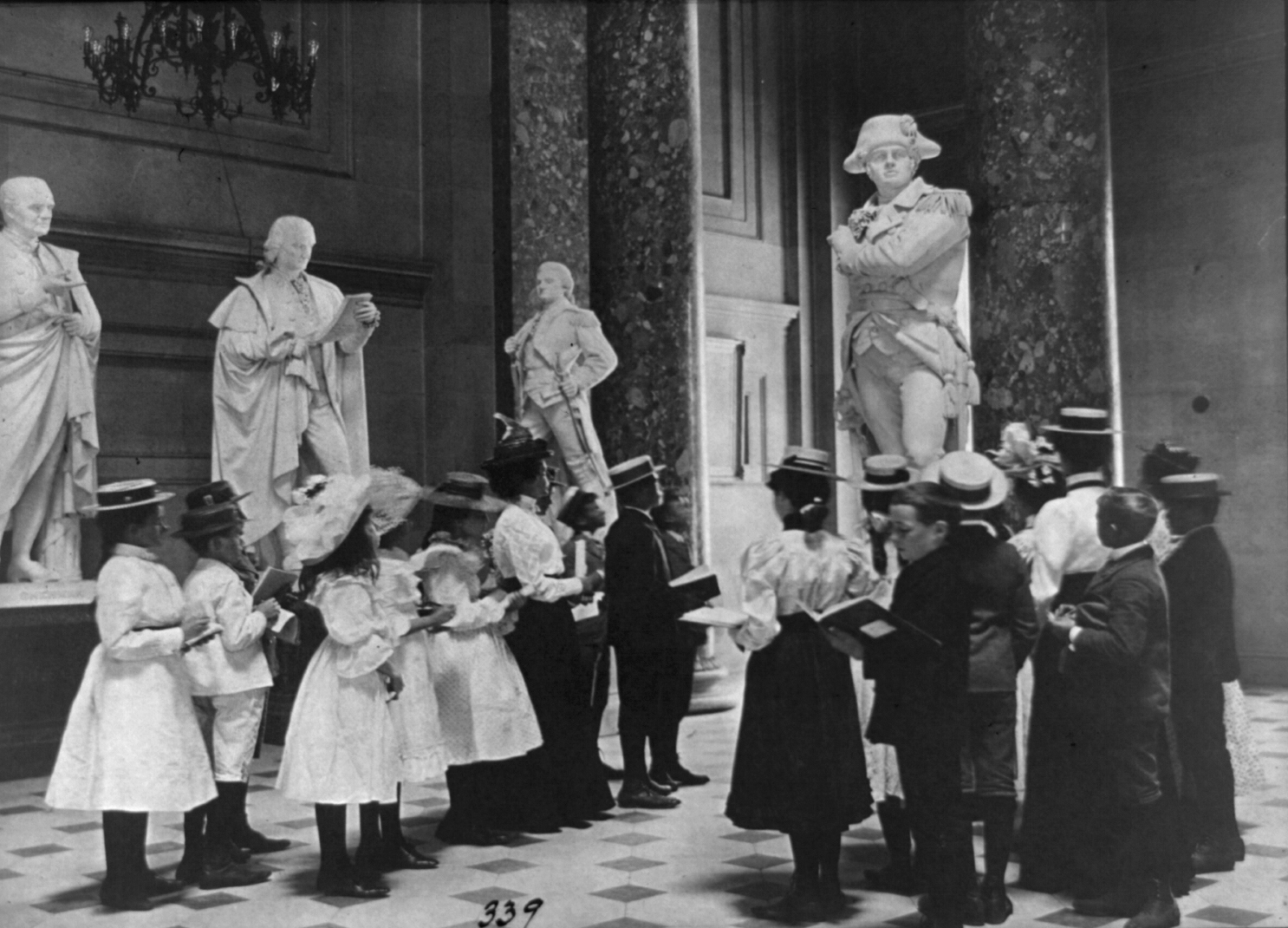 A teacher with students look at a marble statue in National Statuary Hall