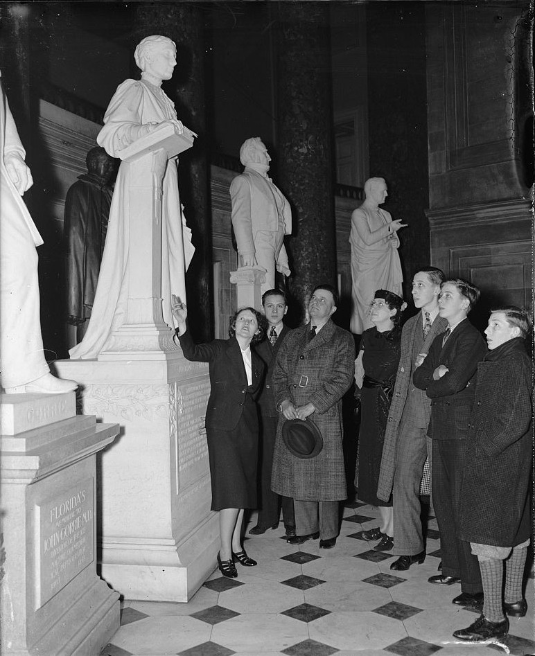 Black and white photo of a woman with a group of people looking at a statue