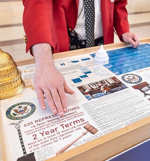 Visitor Guide wearing a red blazer gesturing at cart program materials