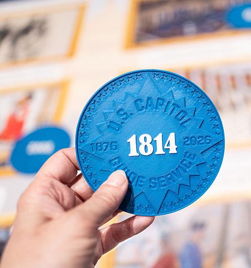 hand holding a large blue circular token with 1814 printed in white in the center 