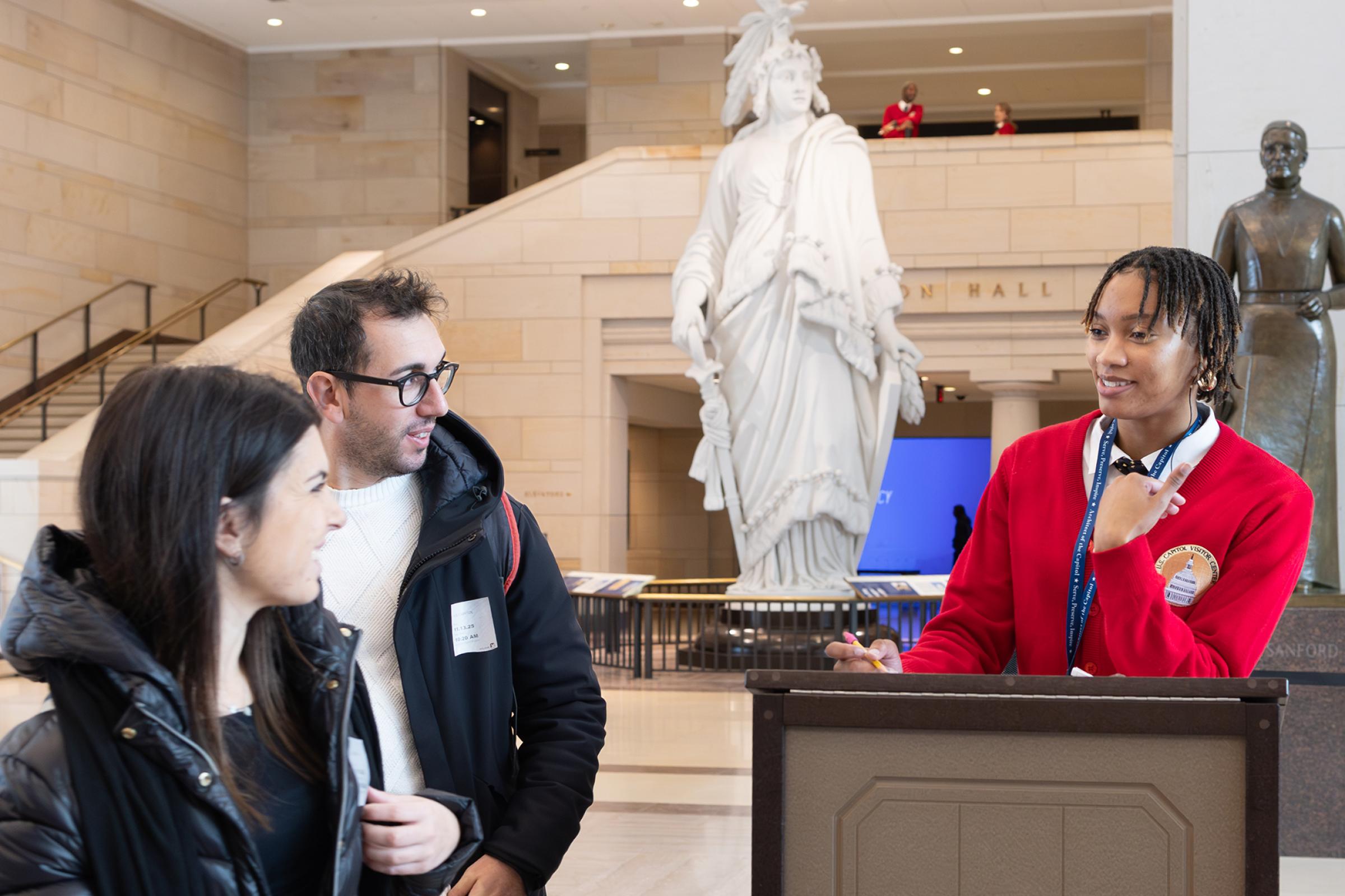 A visitor assistant in a red sweater helps guests.