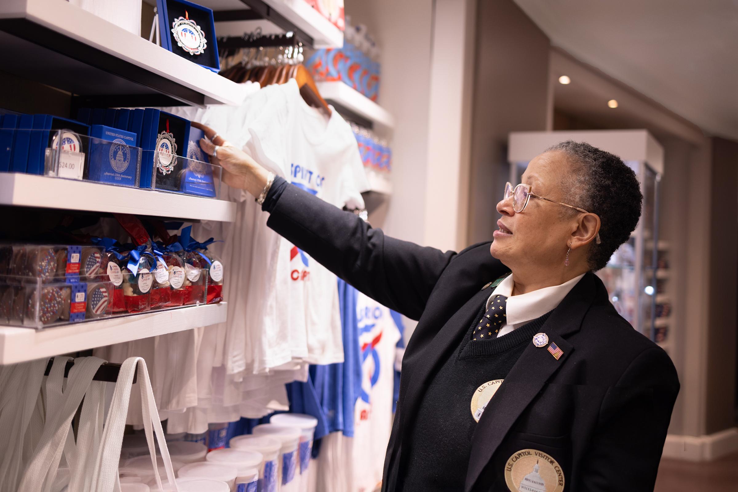 Woman in a black suit with Capitol Visitor Center logo adjusts an ornament for sale in the Gift Shop