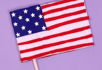 handmade American flag on a light purple background; the flag is crafted from red, white and blue felt attached to a miniature wooden stick 