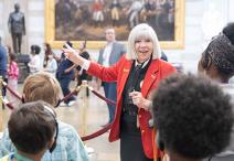 Visitor Guide in a red blazer gestures to a painting behind her in the Capitol Rotunda