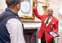 Visitor Guide in a red blazer pointing upwards