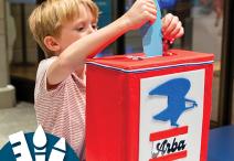 a child drops a blue paper feather into a red Arba mailbox