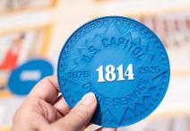 hand holding a large blue circular token with 1814 printed in white in the center 