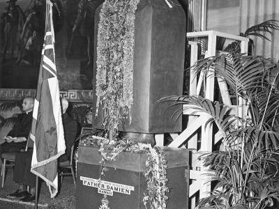 statue that has a name at the bottom stand and is sitting in front of a large painting in the background