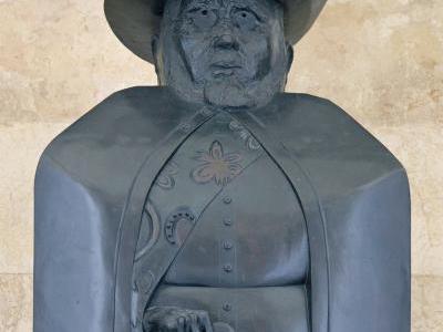 grey statue of a man with a hat and cloak