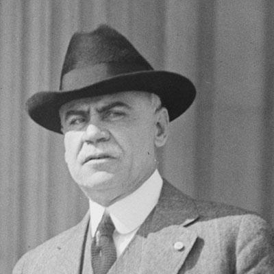 A black and white photo of a man in a hat and suit.