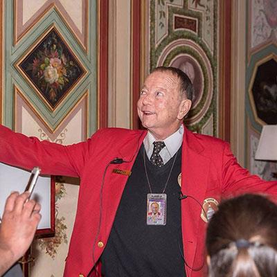 Visitor Guide wearing a red blazer gesturing with both arms spread wide