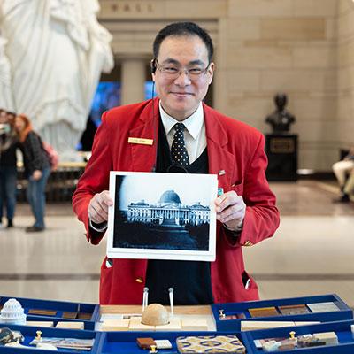 Visitor Guide in a red blazer holding up a vintage photo of the U.S. Capitol