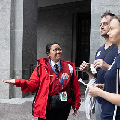 Visitor Guide wearing a red rain jacket gestures to two visitors