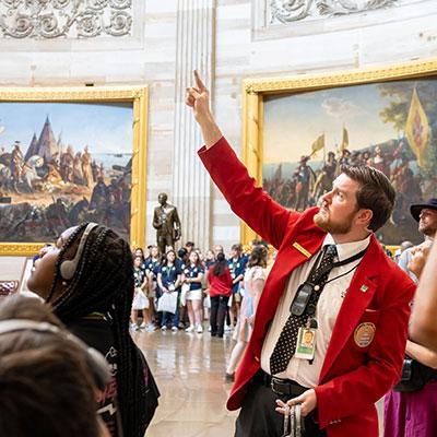 Visitor Guide wearing a red blazer points up towards the ceiling in the Capitol rotunda