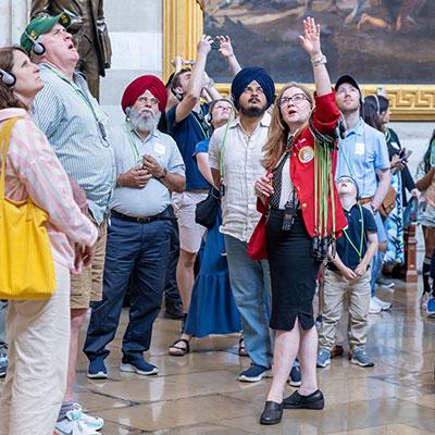 Visitor Guide wearing a red blazer holds a hand up towards the ceiling in the Capitol rotunda