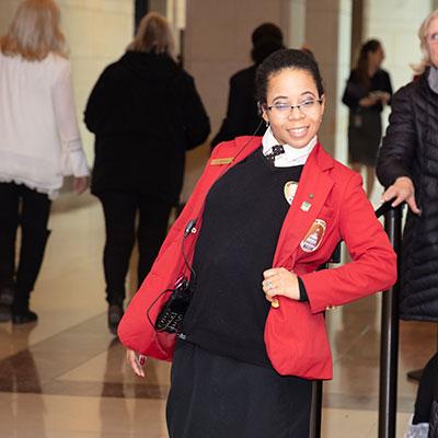 Visitor Guide wearing a red blazer and posing with their left hand on their hip