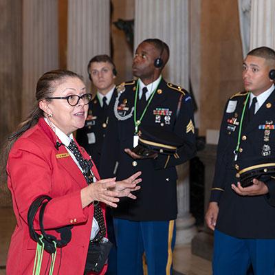 Visitor Guide wearing a red blazer speaks to uniformed servicemembers